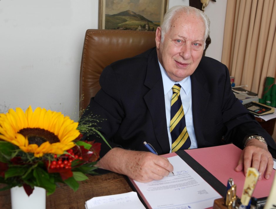 Otto Geilenkirhcen unterschreibt ein Dokument und lächelt.