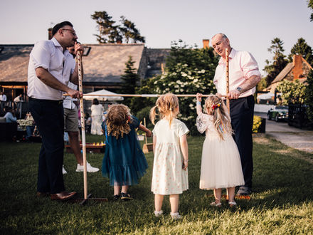 3 young girls stand looking upwards at their dads holding a limbo