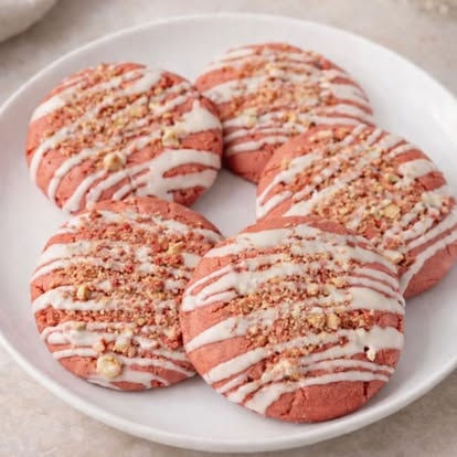 Five pink cookies drizzled with white icing and crushed nuts on plate.