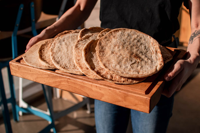 Fresh Pita bread lined up on a wooden tray and held by two hands