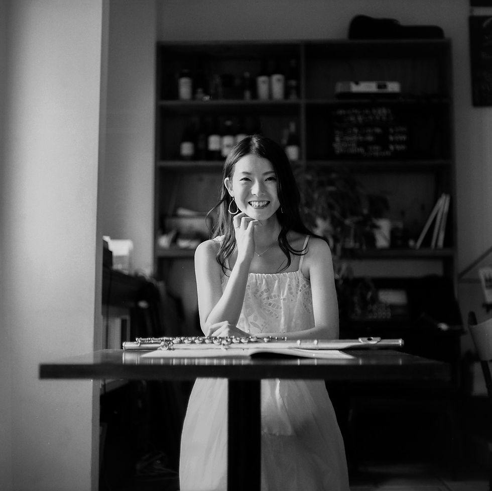 イタリアンレストランのテーブルに肘をついてこちらを見つめ微笑むフルート奏者の女性