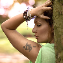 Female model in a green shirt with a bokeh background posing next to a tree. Portrait shot with Canon EOS 2000d.