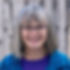 Jo Hawkins - a smiling woman with gray hair and glasses against a blurred wooden fence.
