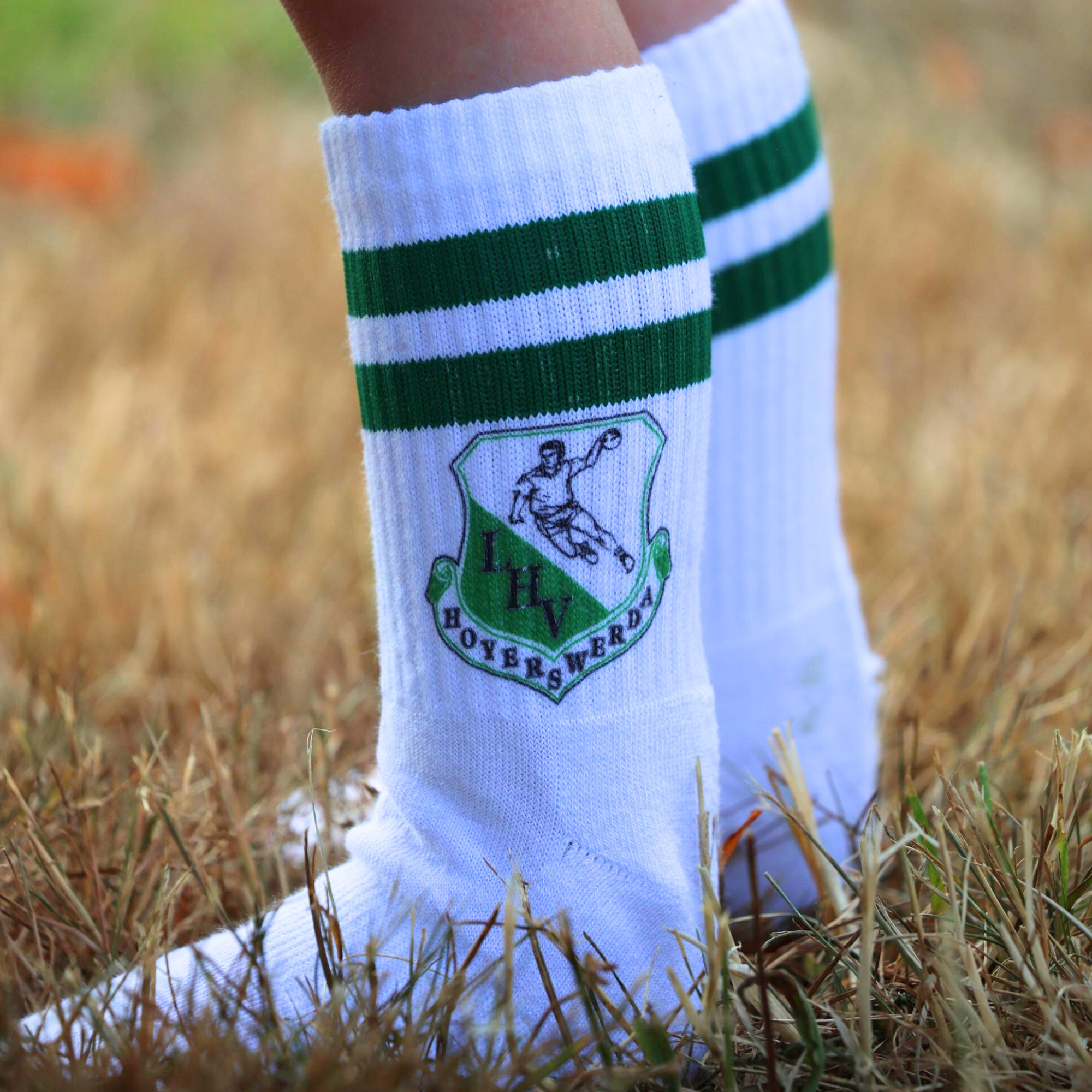 Weiße LHV Socken mit grünen Streifen und aufgedrucktem Vereinslogo, getragen auf einem Rasenplatz