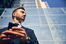 handsome-male-spending-time-alone-near-big-business-center-while-holding-mobile-phone-hand