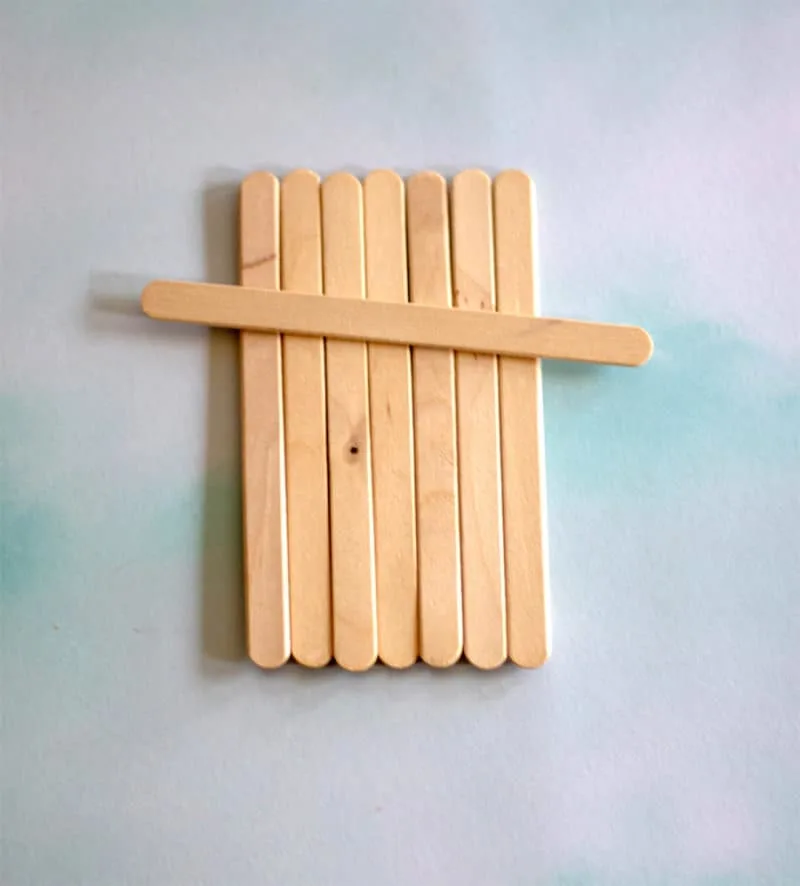 Wooden popsicle sticks arranged vertically with one stick placed horizontally on a light blue background. Calm and simple composition.