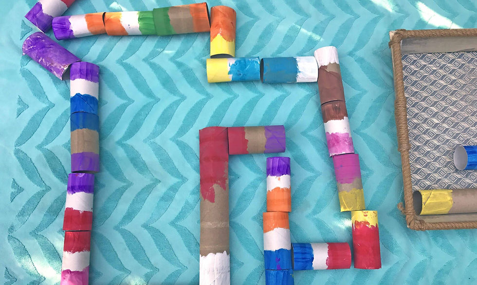 Colorful painted cardboard tubes arranged on a turquoise zigzag-patterned surface, alongside a rope-edged tray.