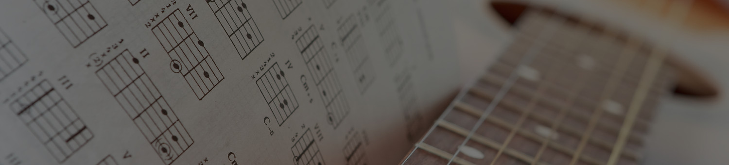 Open book of guitar chord diagrams next to a classical guitar fretboard, representing Guitarra Music Academy's structured approach to learning guitar