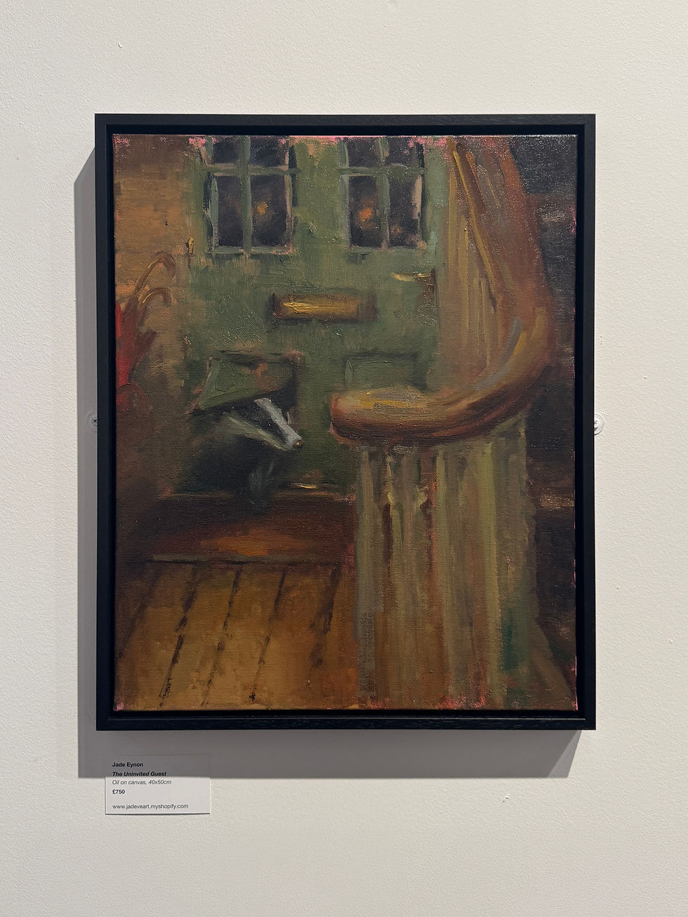 This painting has a black frame around it and is of a green door with a badger poking their head through a cat flap. There are hints of a hallway with a wooden panelled floor and a red umbrella sat by the front door. Front of the painting is the beginning of the stairs with a curved hand rail peeking in from the right.