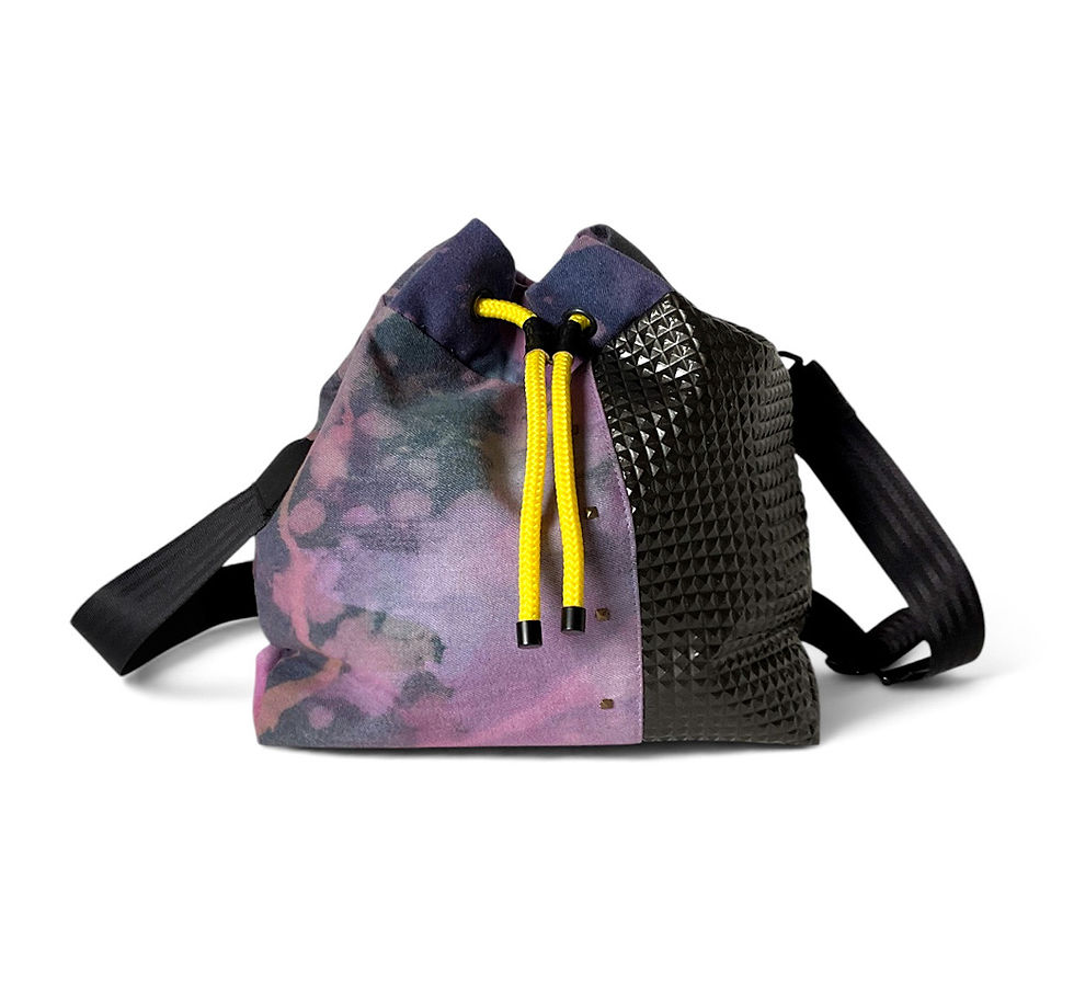 Ein Beuteltasche mit Kordelzug, der auf einer Seite einen violett-blauen Batikstoff und auf der anderen Seite ein schwarzes,