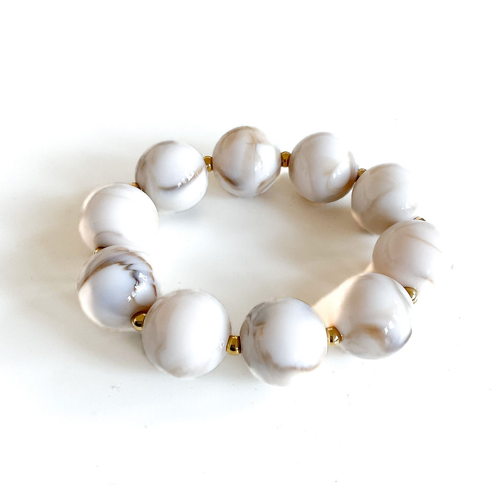 Ein Armband aus weißen und hellbraun marmorierten Perlen. Das Armband hat große, runde Perlen mit goldfarbenen Abstandshalter