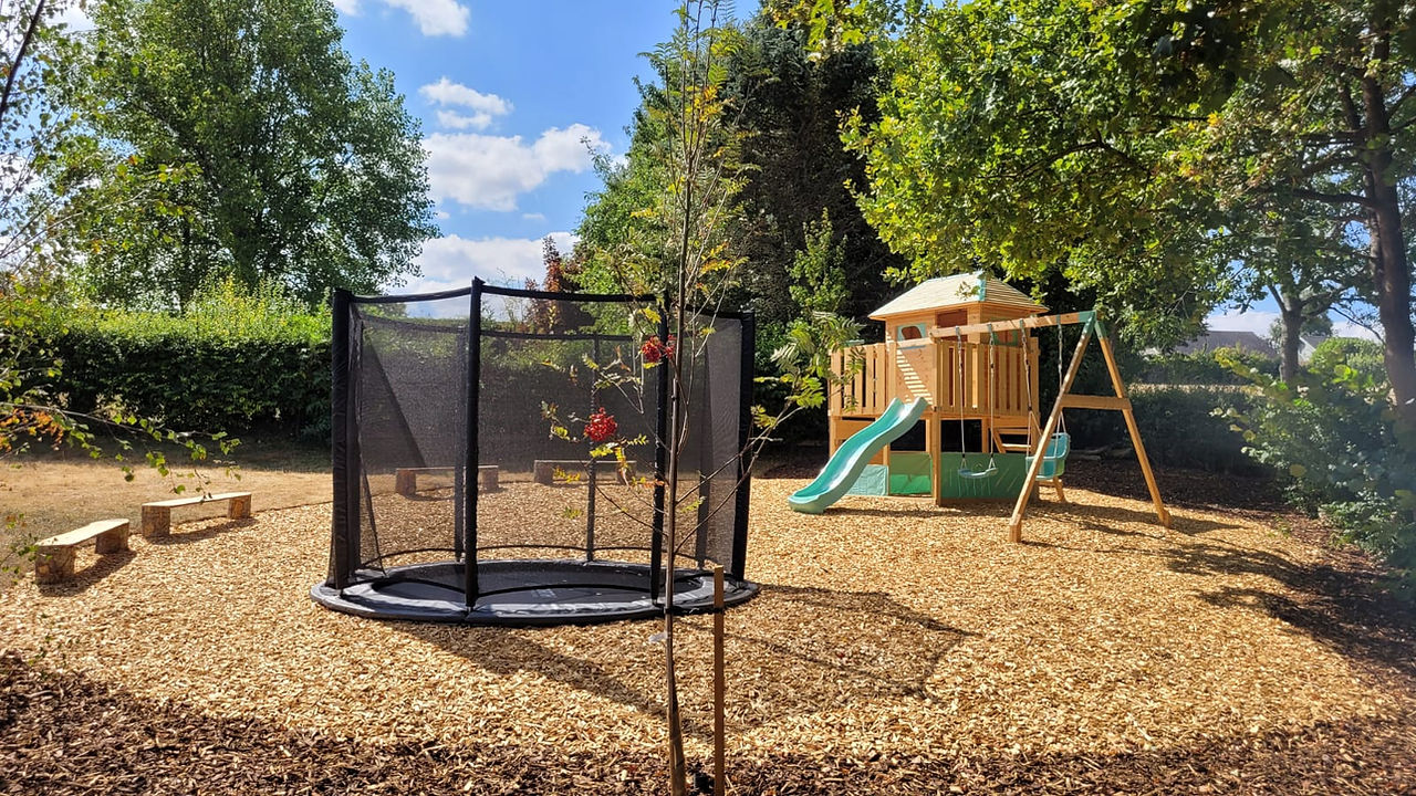Sunken trampoline and timber play structure in a bark play area near Chipping Norton