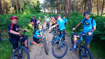 a group of around 15 mountain bikers gathered together on a woodland trail.