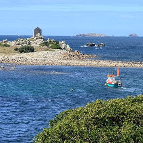 Sailing boats anchored in clear blue water near rocky islands on the Isles of Scilly coastline.