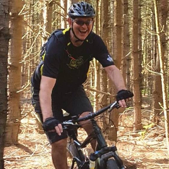 A photo of steve coombs, smiling, on his mountain bike on a woodland trail. he is the owner of steve coombs mountain bike skill training.