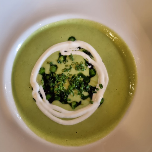 A beautifully presented bowl of bright green pea soup with a delicate cream swirl, served at a Michelin-level restaurant on Saaremaa Island, Estonia.
