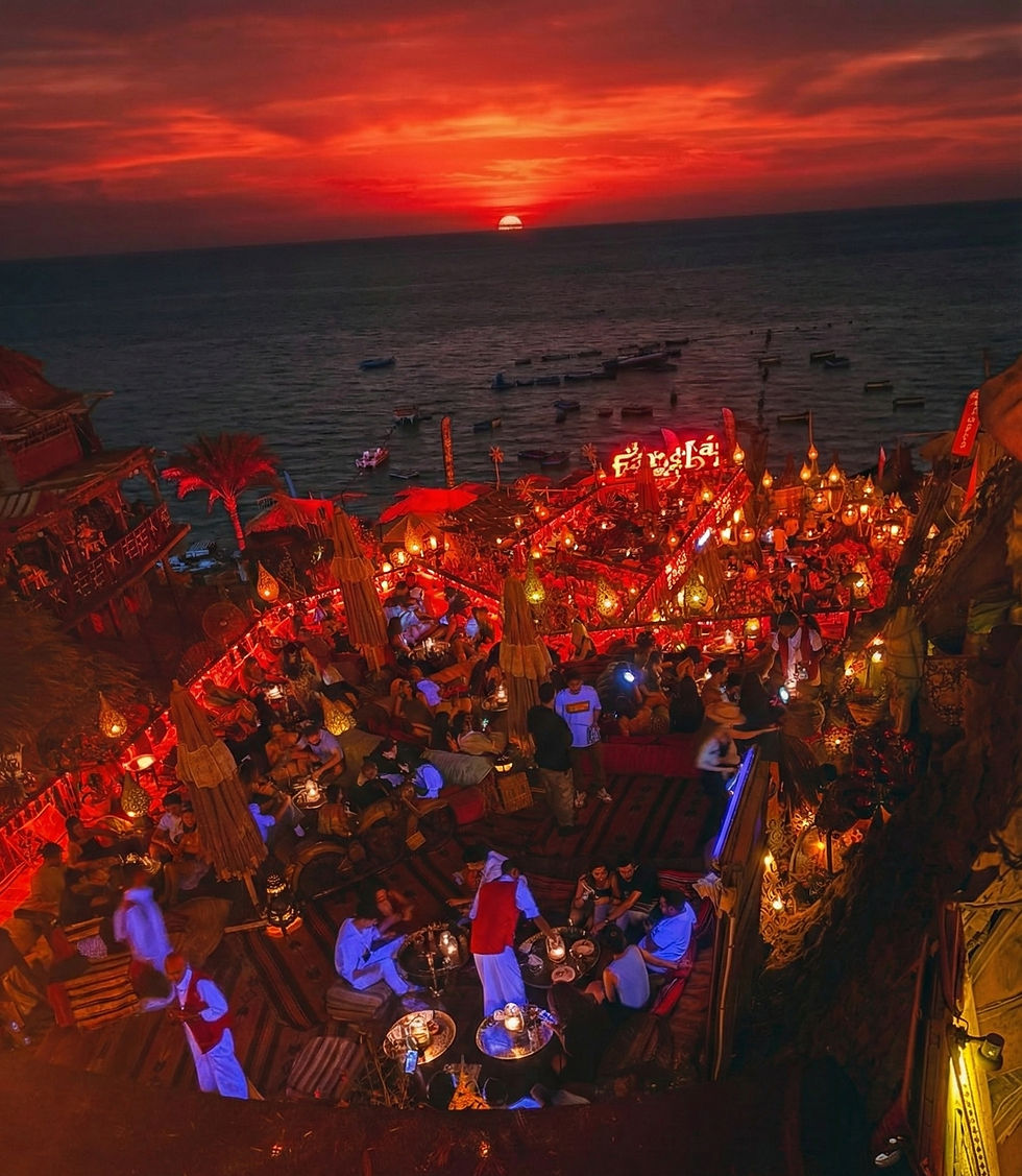 An overhead shot of the Farsha Mountain Lounge in Egypt, capturing a stunning red sunset, the sea, and the various levels of the lounge, with lots of guests, beautiful lighting.