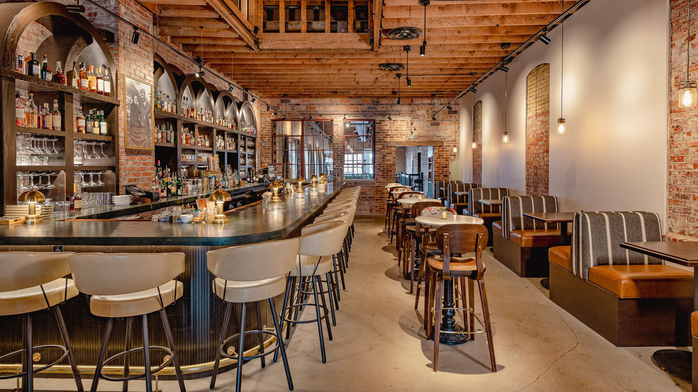 Lounge at Myrtle’s with curved cocktail bar, barstools, and booth seating along exposed brick wall — available for private dining, wedding receptions, and full venue events in Sioux Falls