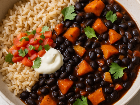 A bowl of hearty black bean and sweet potato stew served with brown rice, topped with fresh pico de gallo, a dollop of sour cream, and garnished with cilantro leaves.