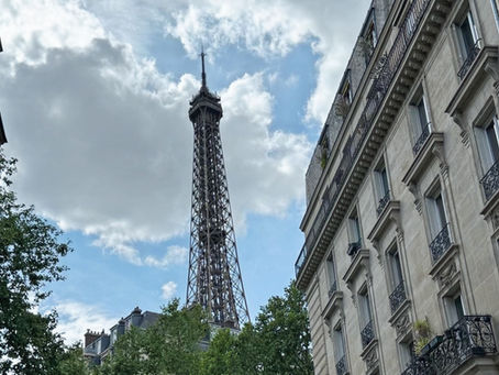 The Eiffel Tower rises behind the historic American Library in Paris, nestled among elegant Haussmann-style buildings. A quiet street scene captures the blend of literary legacy and iconic French beauty.