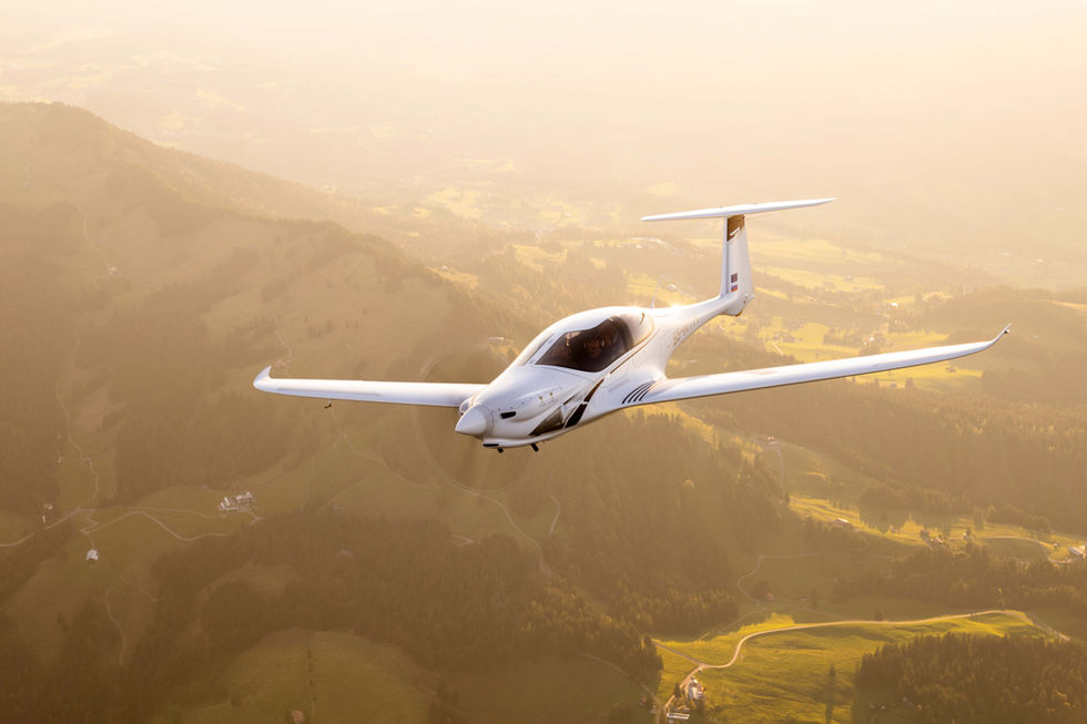 Pipistrel Panthera aircraft inflight in a right bank angle, backlit, above greenish hills, air to air photo by Samy Kramer