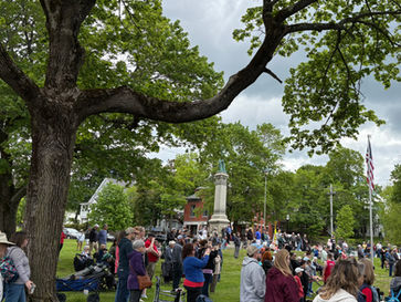 Veterans in uniform sit in front of a high school marching band during a solemn Memorial Day ceremony