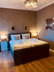 Blick ins Schlafzimmer mit Doppelbett und angeschalteten Nachttisch-Lampen