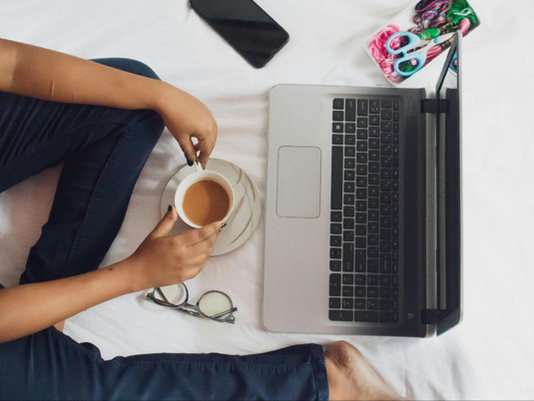 Person's hands around cup of coffee while at a laptop