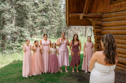 Bridesmaids reacting emotionally to bride reveal outside log cabin
