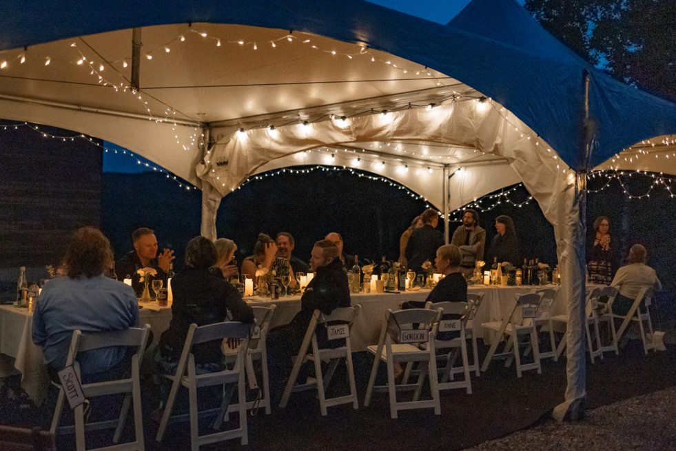 Candlelit reception dinner under a tent with guests sharing conversation and laughter at an intimate wedding