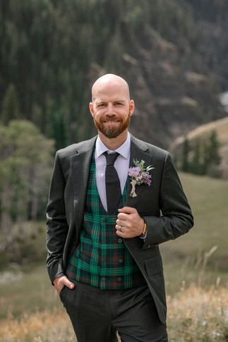Classic elopement ideas groom portrait in a dark suit with a green tartan vest and boutonniere in a mountain valley