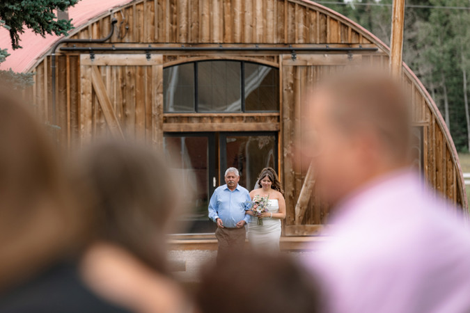 Bride walking down the aisle with her father toward rustic ceremony space during Bragg Creek wedding at Folk Tree Lodge