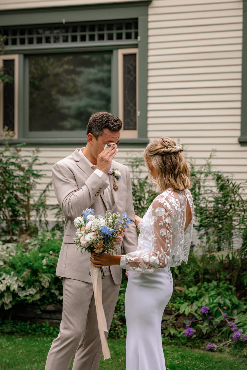 Emotional moment during first look wedding photos as groom wipes away tears while holding bride’s bouquet.