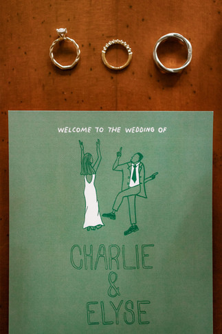 Flat lay of wedding rings arranged above a custom illustrated wedding program during Calgary wedding planning.