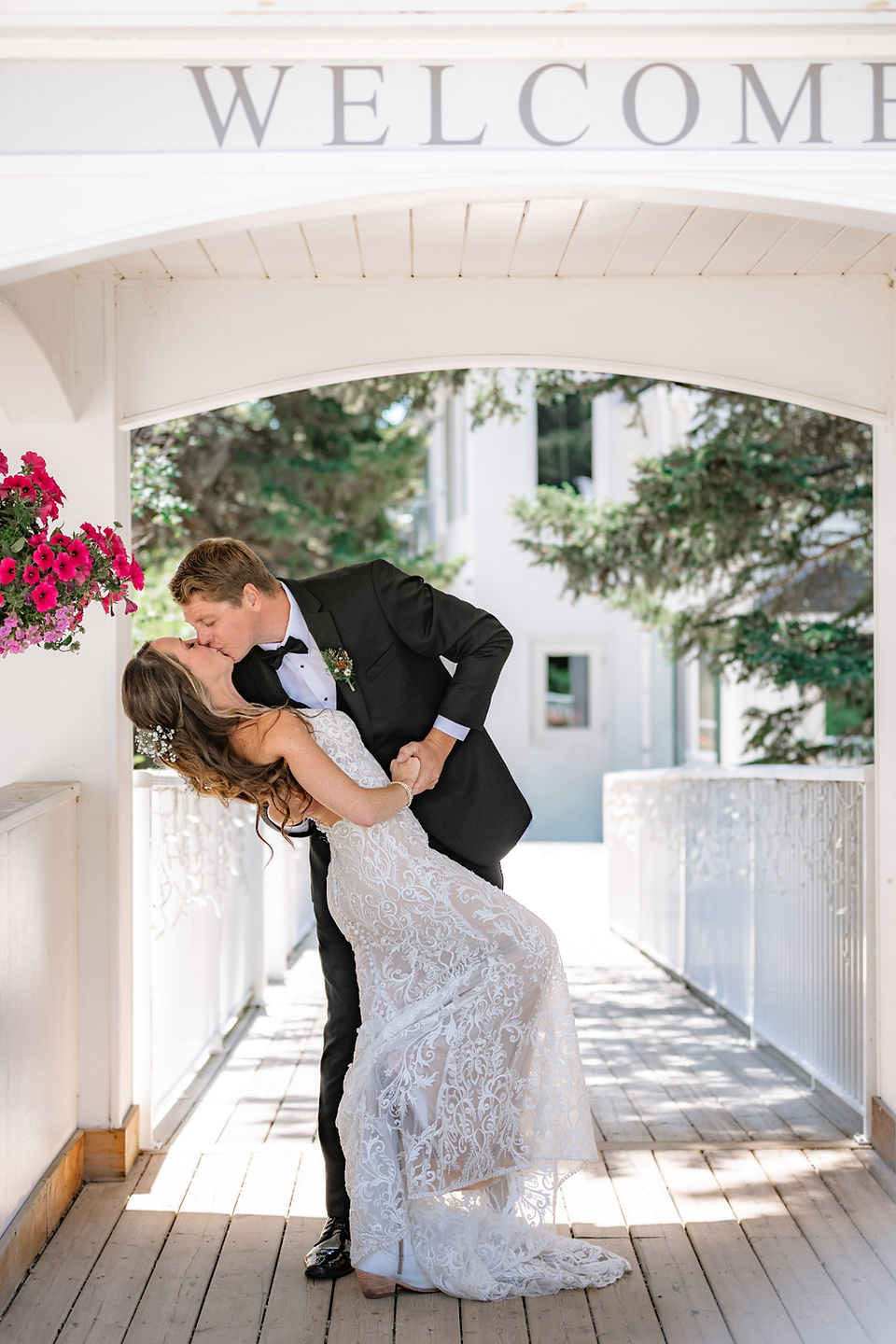 Bride and groom sharing a romantic dip kiss under a white archway at a rustic outdoor wedding venue