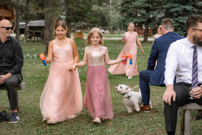 Flower girls walking down aisle blowing bubbles with playful energy during outdoor ceremony