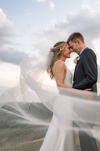 Bride and groom sharing an intimate forehead touch with flowing veil during sunset portraits after hiring a wedding videographer in Calgary