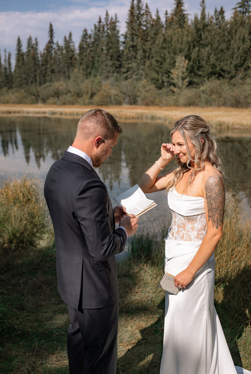 candid wedding photography for weddings capturing a groom reading vows as the bride wipes away happy tears by the water