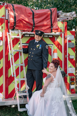 Bride and groom posing with a fire truck, featuring a firefighter groom in uniform