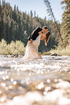 Groom dipping bride in a sparkling river surrounded by trees, showcasing romantic Calgary small wedding venues