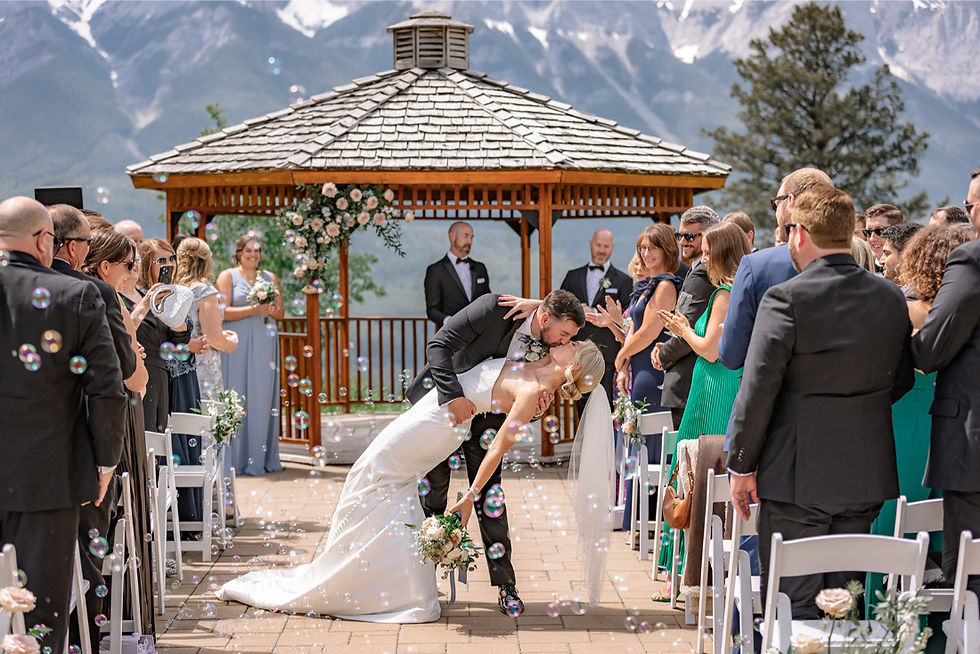 Bride and groom sharing a joyful ceremony kiss under a floral arbor with mountain views during Calgary wedding planning at an outdoor venue
