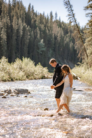 Newlyweds walking barefoot through a shallow river in a forest setting, perfect for Calgary small wedding venues