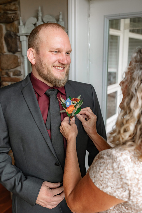 Groom smiling as a boutonniere is pinned, photographed by a destination wedding photographer during wedding day preparations.