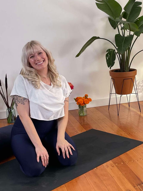 Prenatal yoga teacher Emily Rae sits on mat smiling with nearby student Dusti