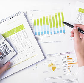 Printed financial charts and graphs spread across a desk, with a hand holding a pen over them.