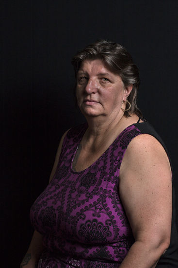 Woman poses in front of black background with visible purple top.