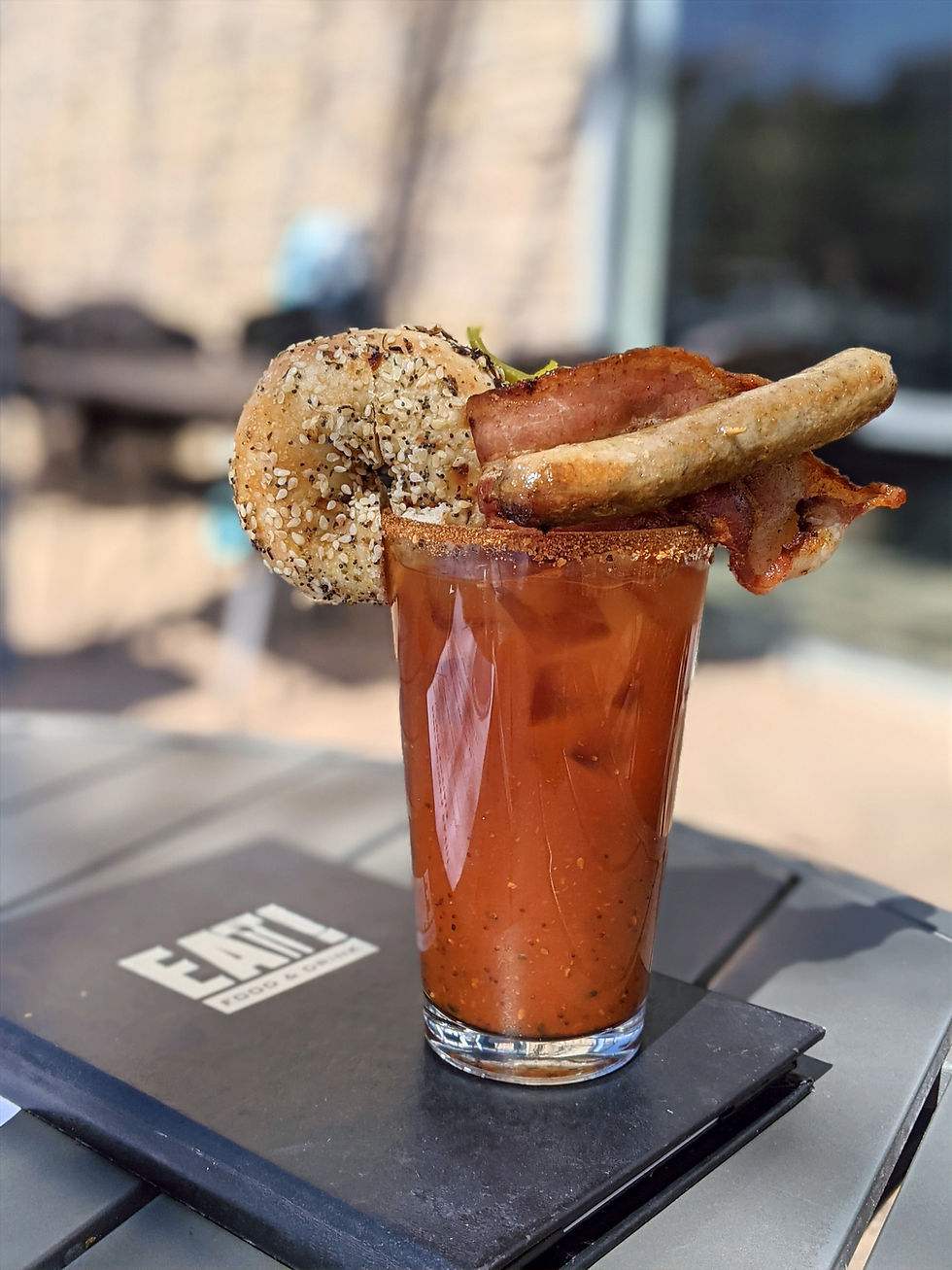 Bloody mary garnished with sausage, bacon, and a mini everything bagel