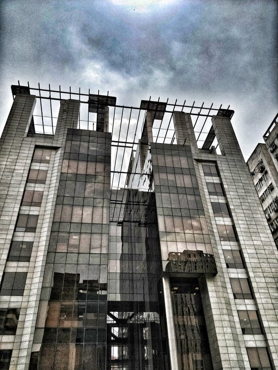 An image of a derelict building against a cloudy gray sky. The iron structure of the building is exposed, and it is visibly degrading,