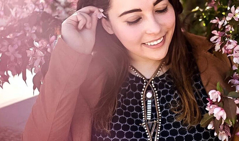 An image of Kelli Lage, a person with long brown hair raising a hand to her ear and smiling.