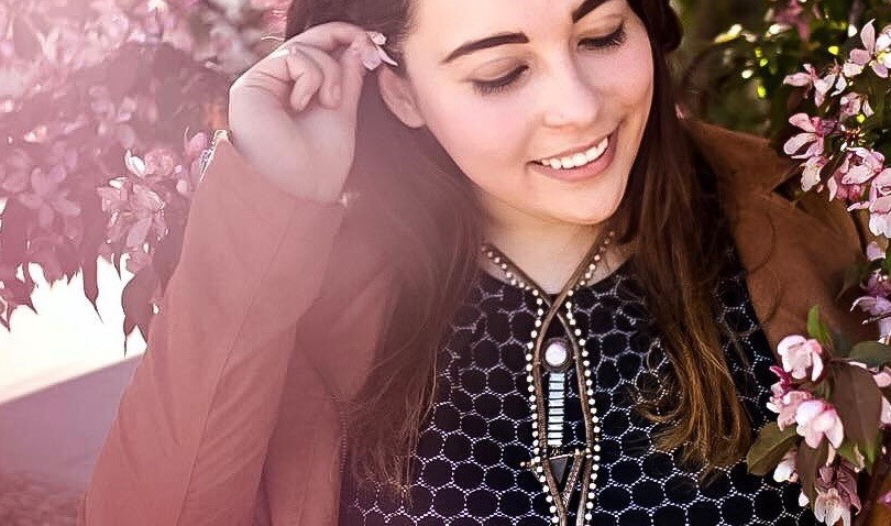 An image of Kelli Lage, a person with long brown hair raising a hand to her ear and smiling.